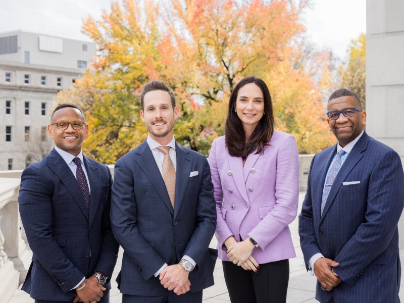 Close up team photo of Rodney, Kate, Brian, and Kelvin, standing near a courthouse with a tree behind them.